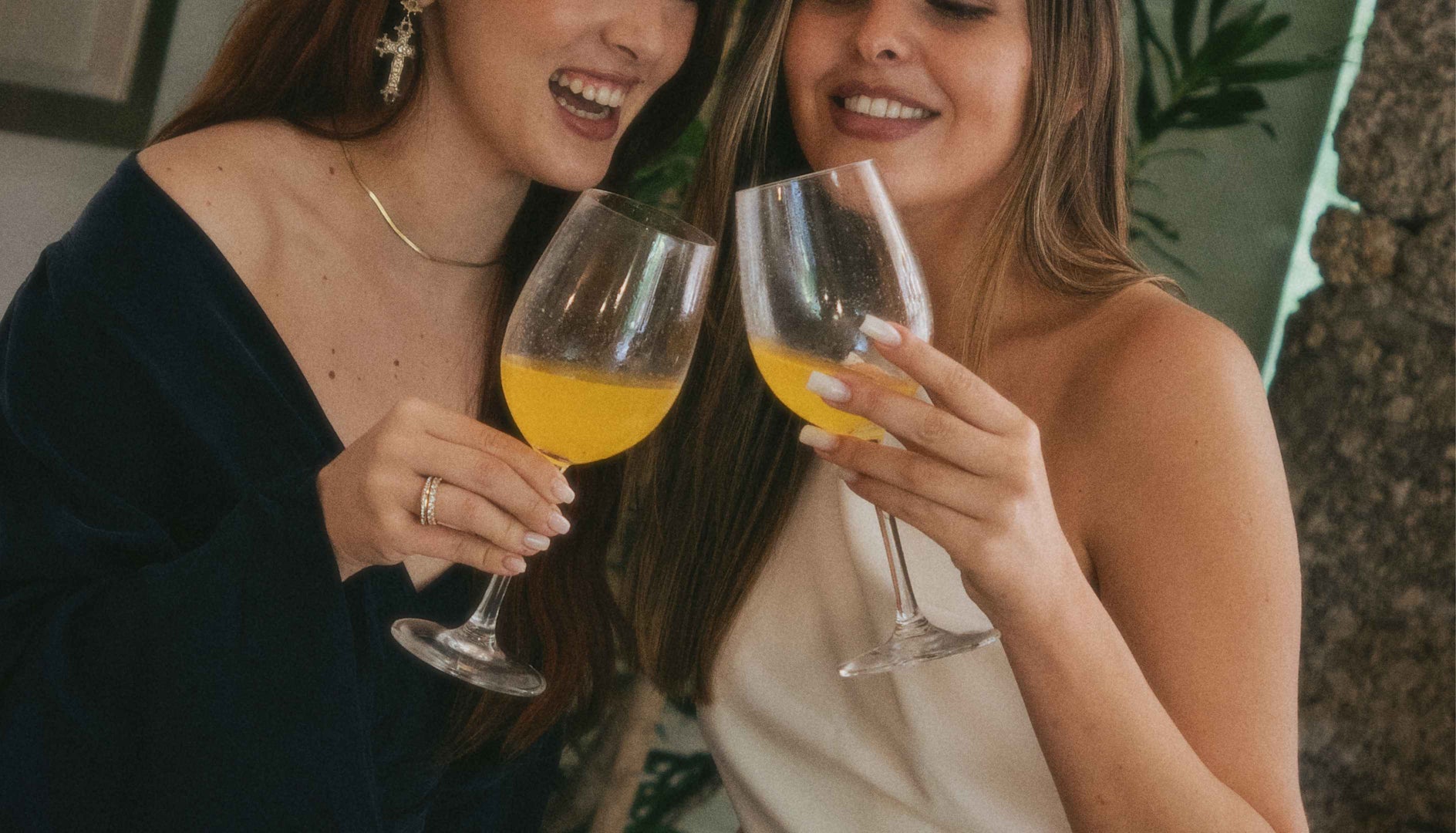 Duas mulheres a sorrir e a  brindar com copos de sangria de maracujá