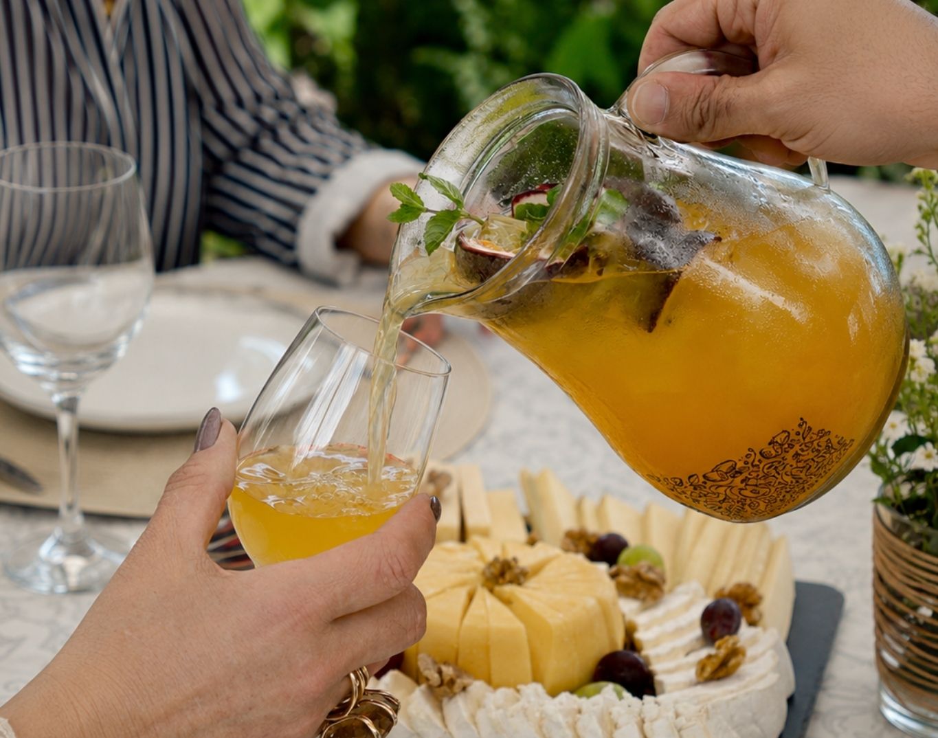 Pessoa a servir sangria de maracujá BOUA Esencia num copo junto a uma tábua de queijos
