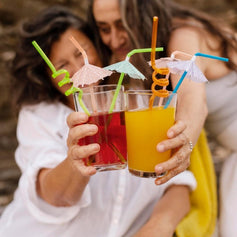 Duas mulheres a brindar com bebidas coloridas ao ar livre