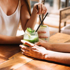 Duas pessoas a beber cocktails frescos numa mesa de madeira ao sol