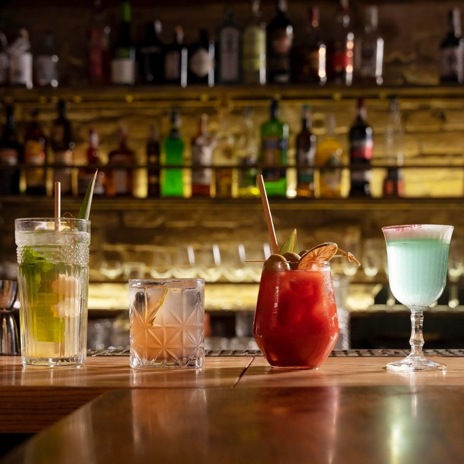 Vários cocktails coloridos servidos num balcão de um bar