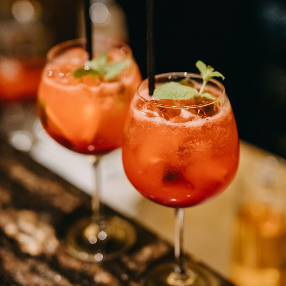 Cocktails vermelhos com gelo e hortelã servidos em copos de pé