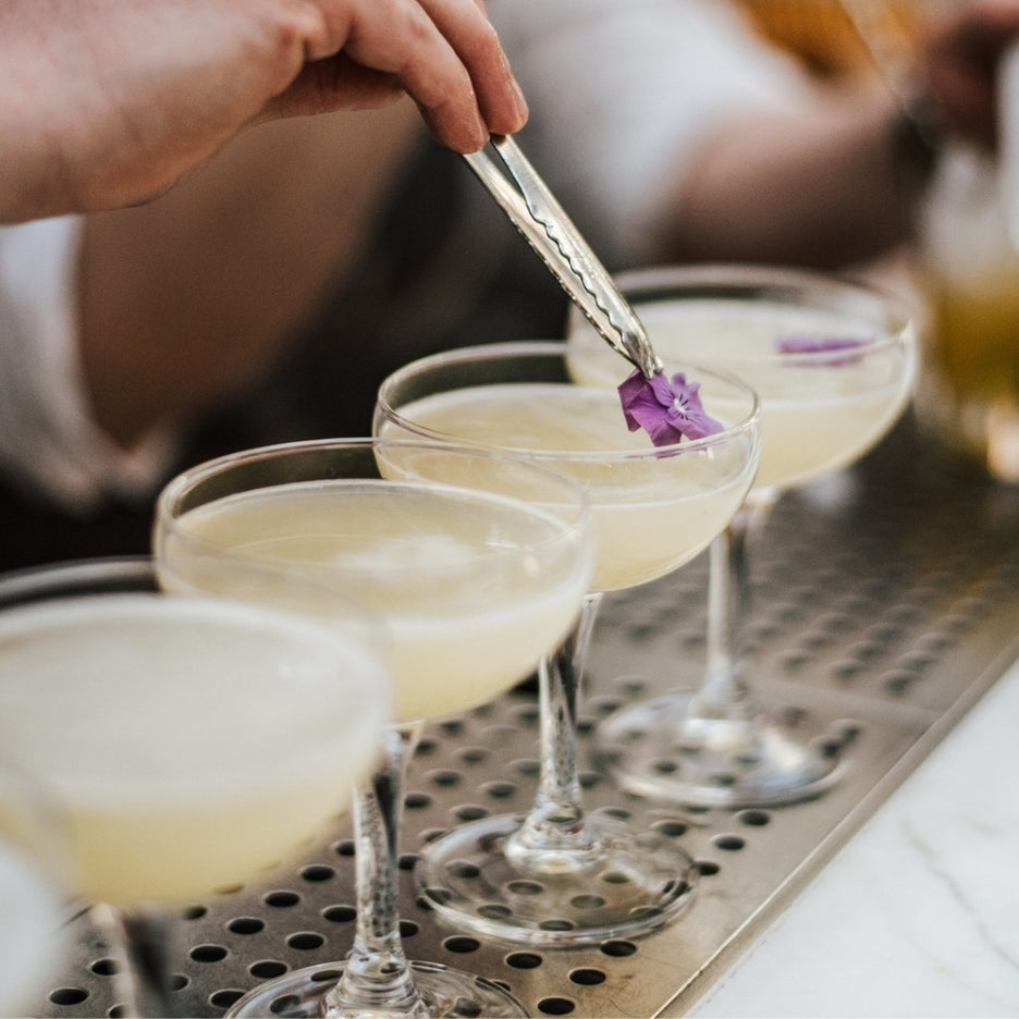 Copos de mocktail finalizados com flor comestível sobre balcão de bar